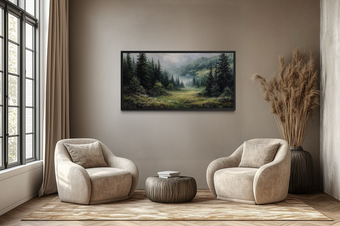 Misty mountain meadow and pine forest canvas wall art in a black frame above two beige armchairs.