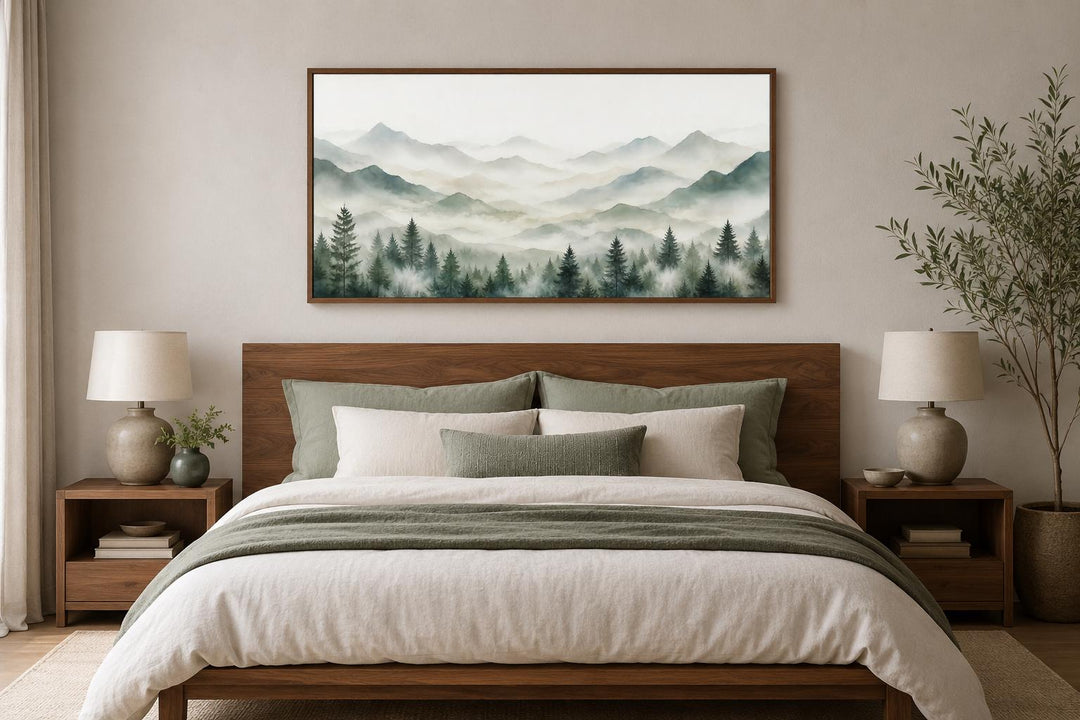 Misty mountain and sage green pine tree canvas painting framed above a bed in a neutral bedroom.