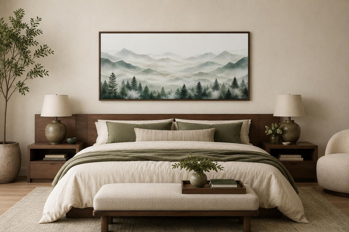 Misty mountain painting with sage green pine trees on canvas above a bed in a neutral bedroom.