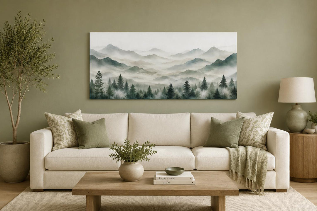 Misty mountain and sage green pine tree canvas art hanging above a sofa in a neutral living room.