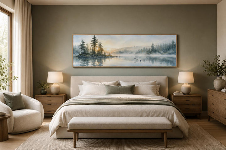 Panoramic misty pine forest and lake canvas wall art hanging above a bed in a neutral bedroom.