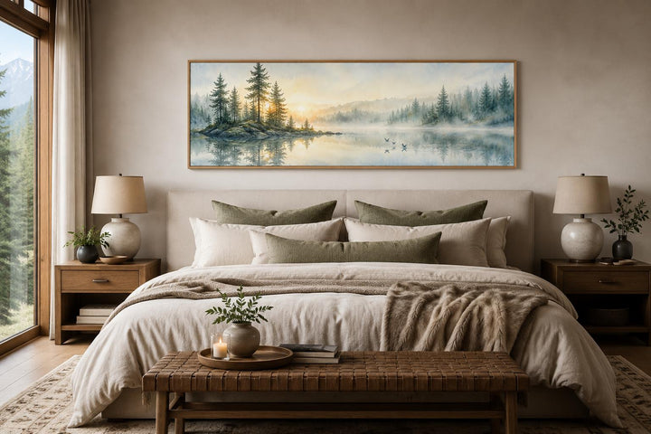 Panoramic misty pine forest and serene lake canvas print hanging above a bed in a neutral bedroom.