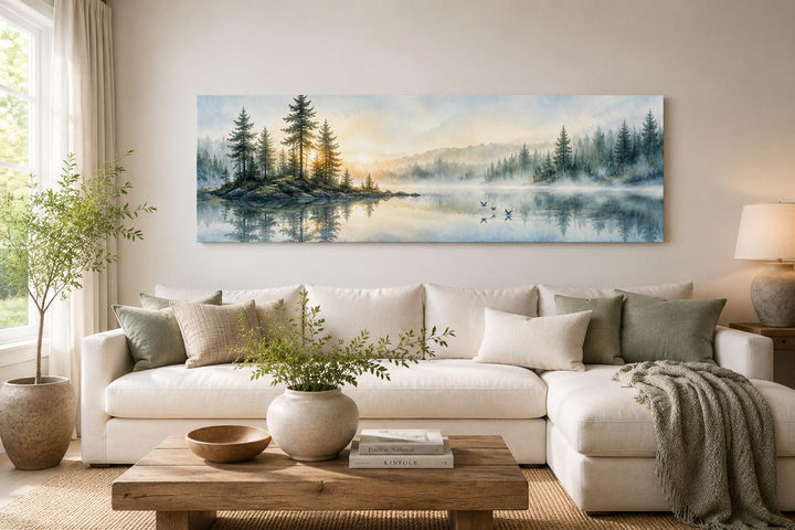 Panoramic misty pine forest and serene lake canvas print above a white sofa in a neutral living room