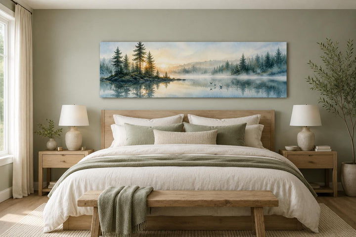 Panoramic misty pine forest and lake canvas print hanging above a bed in a neutral-toned bedroom.