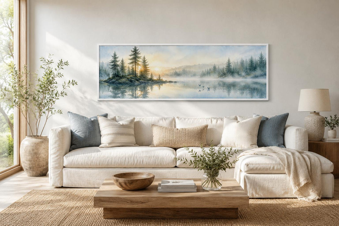 Panoramic misty pine forest and lake canvas print hanging above a white sofa in a neutral room.