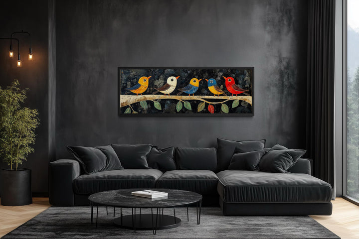 Modern folk style canvas art of colorful birds on a branch above a black sofa in a dark room.