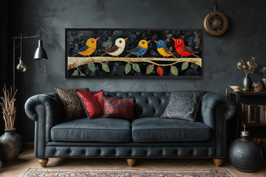 Modern colorful folk style birds on a branch long narrow canvas wall art above a dark blue sofa.