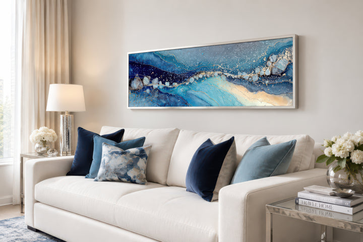 Modern long horizontal blue and navy abstract canvas art above a white couch with blue pillows.