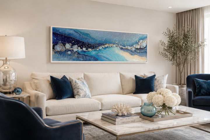 Modern long horizontal blue and navy abstract canvas art hanging above a white sofa.