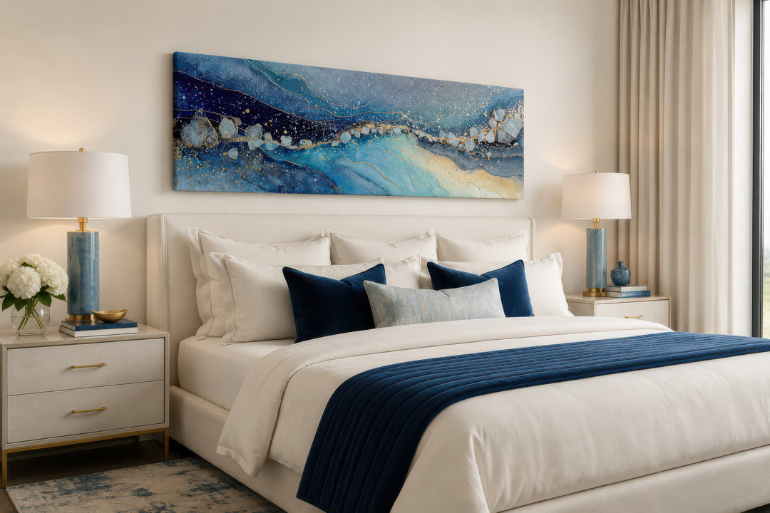 Modern long horizontal blue and navy abstract canvas art hanging above a bed in a neutral bedroom.