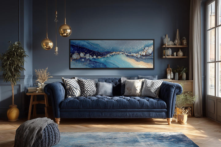 Modern long horizontal blue and navy abstract canvas art hanging above a dark blue tufted sofa.