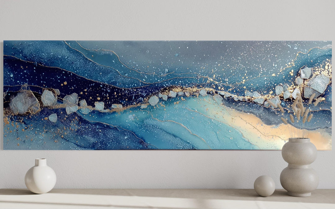 Modern long horizontal abstract canvas art with navy, blue, and gold accents above a console table.