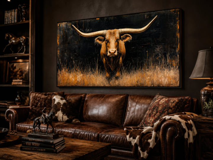 Framed canvas wall art of a Texas longhorn steer in golden grass above a leather sofa.