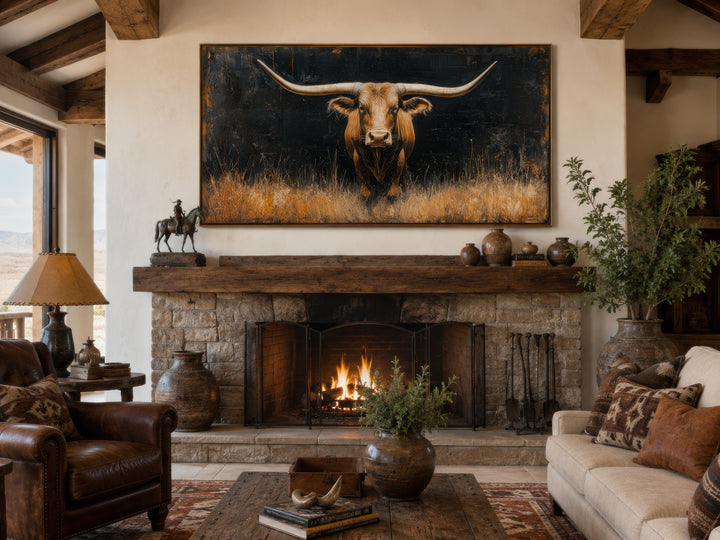 Framed canvas wall art of a Texas longhorn steer in grass above a rustic stone fireplace.