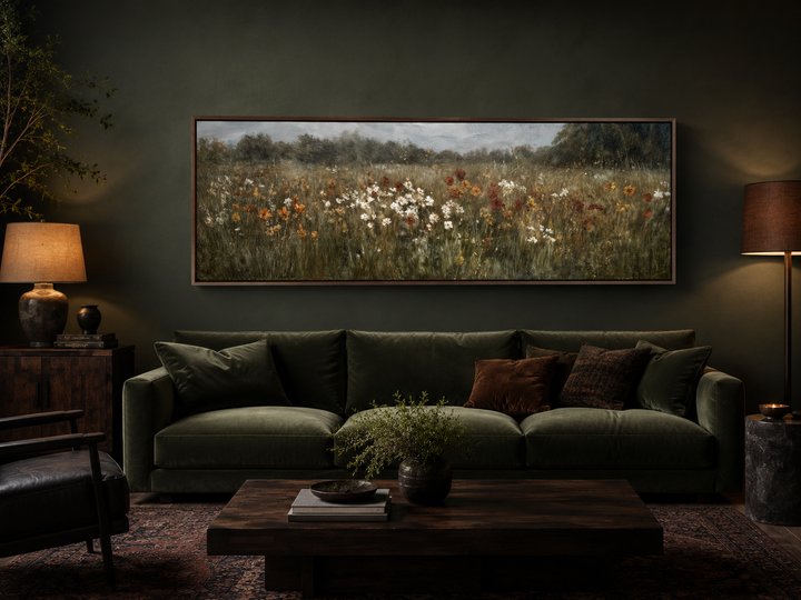Moody muted wildflower field horizontal canvas art above a green velvet sofa in a dark room.
