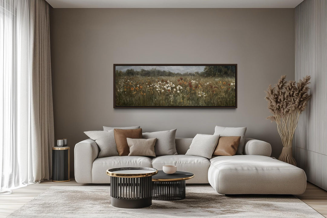 A long horizontal canvas of a muted wildflower field hangs above a modern sofa in a neutral room.