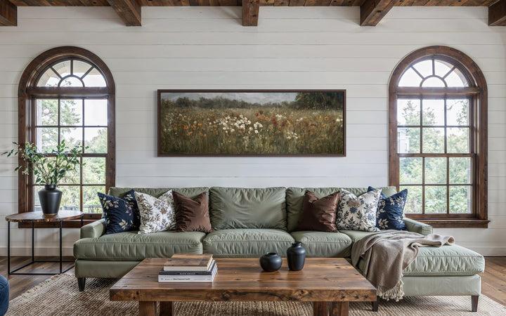 A long horizontal canvas painting of a muted wildflower field hangs above a green sofa.