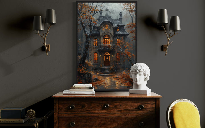 Framed canvas art of a moody Victorian house in a rainy autumn forest above a wooden dresser.