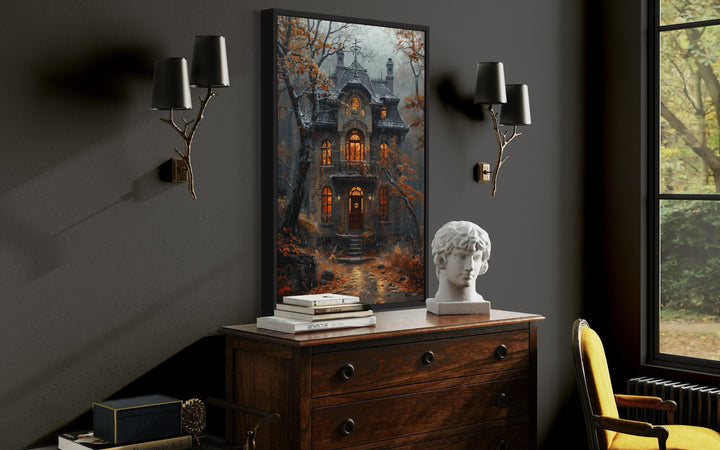 Framed canvas wall art of a moody Victorian house in a rainy autumn forest above a wooden dresser.