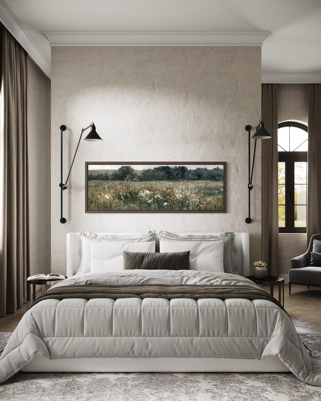A long narrow horizontal painting of a moody wildflower field hangs above a bed in a neutral room.