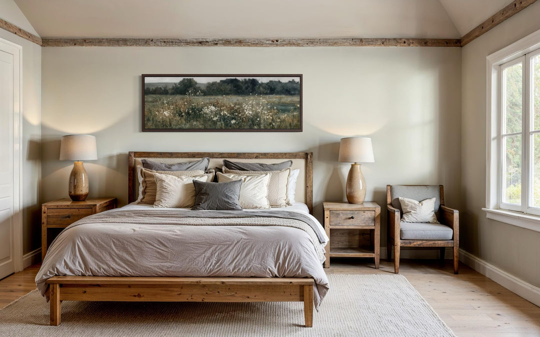 A long narrow horizontal painting of a wildflower field hangs above a bed in a rustic bedroom.