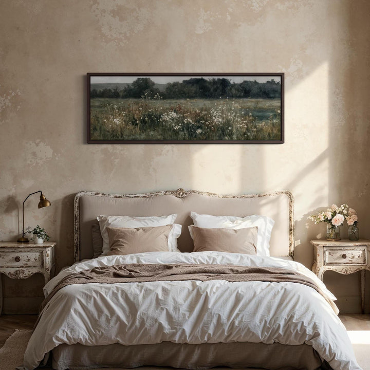A long narrow horizontal painting of a moody wildflower field hangs above a rustic bed.