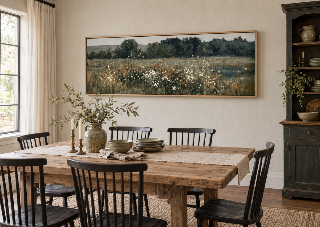 Long narrow horizontal painting of a moody wildflower field above a rustic wooden dining table.