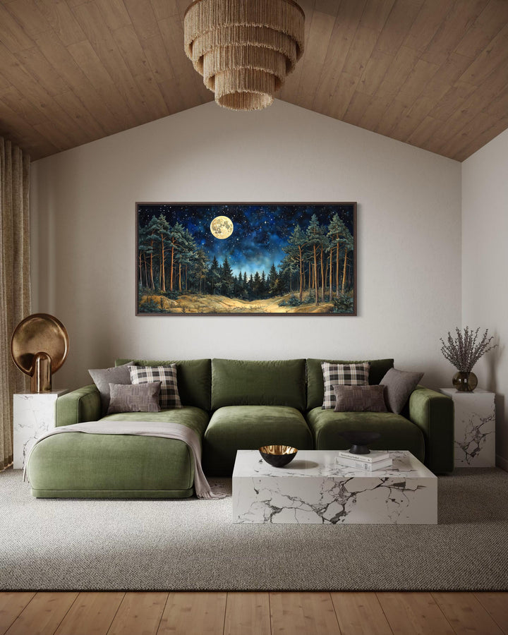 Horizontal wall art of a moonlit pine forest above a green sofa in a modern rustic living room.