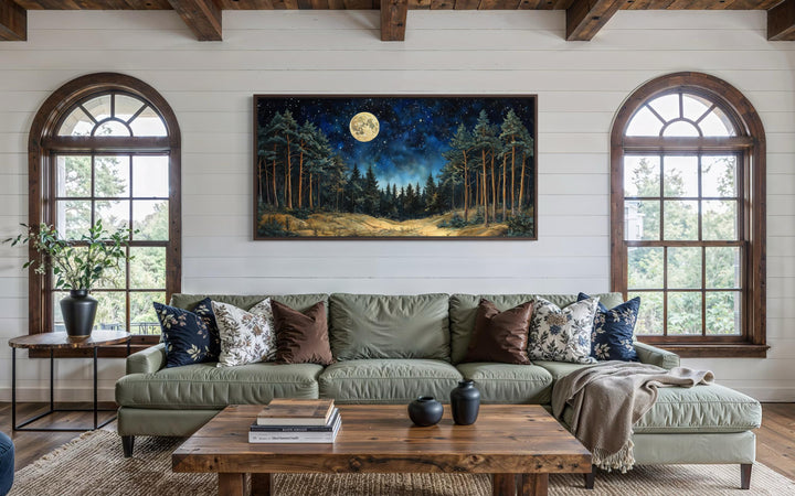 Horizontal wall art of a moonlit pine forest above a green sofa in a rustic living room.