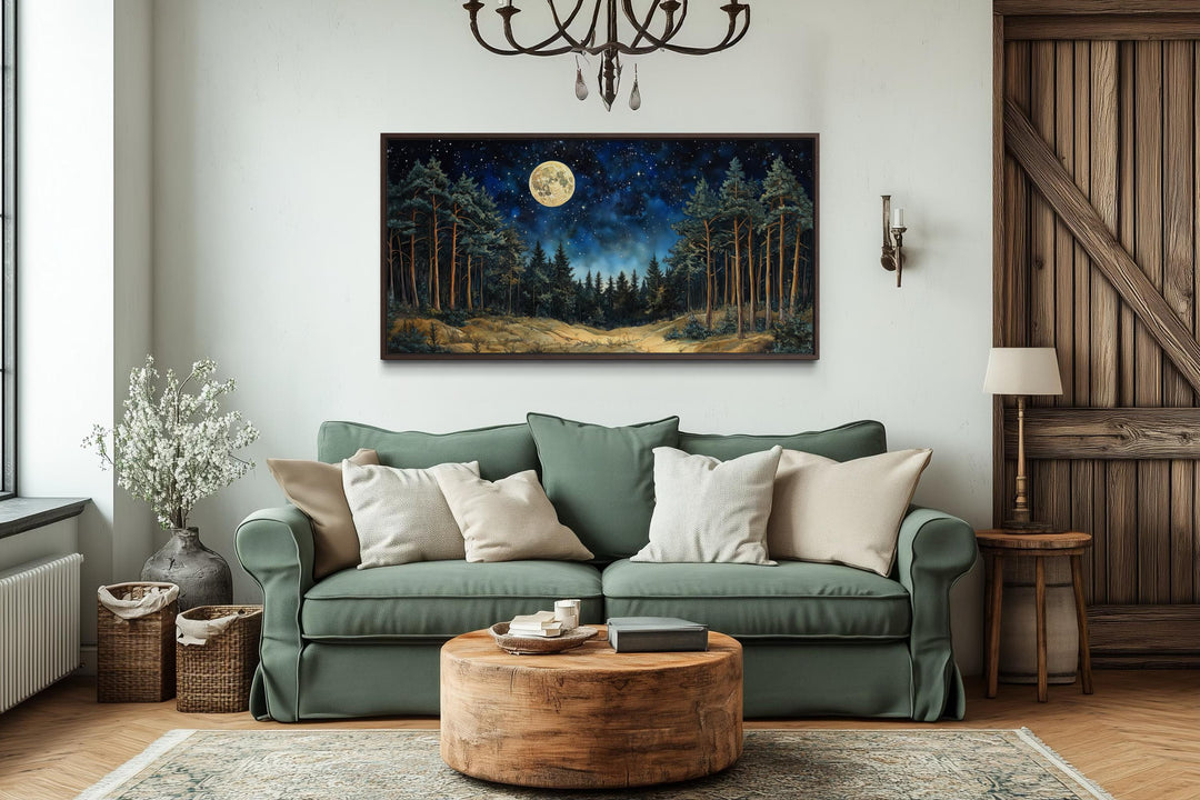 A horizontal canvas print of a moonlit pine forest hangs above a green sofa in a rustic living room.