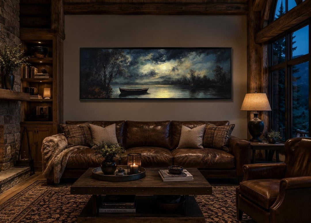 Long narrow canvas wall art of a moonlit rowboat on a still lake, hung above a brown leather sofa.