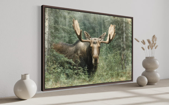 Rustic moose painting on canvas in a dark wood frame, displayed in a minimalist room setting.