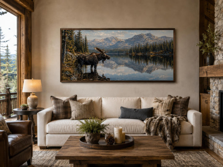 Moose near lake wall art in a rustic living room above a white sofa with mountain landscape.