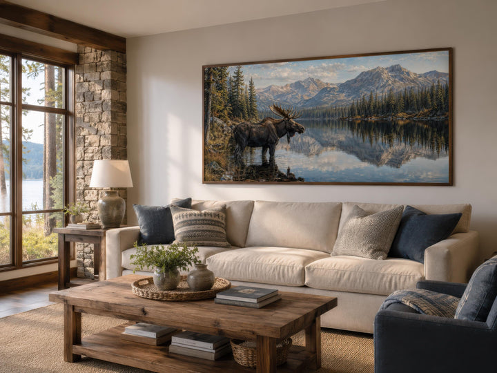 Large horizontal canvas art of a moose in a mountain lake above a sofa in a rustic living room.