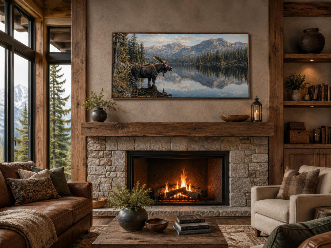 Moose near a lake wall art displayed above a stone fireplace mantel in a rustic living room.