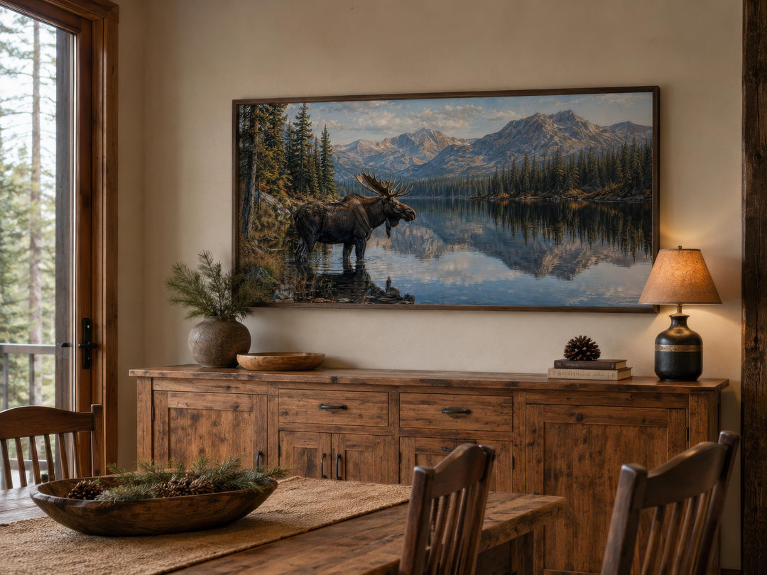 Moose near a lake wall art above a rustic wooden sideboard in a cabin-style dining room.
