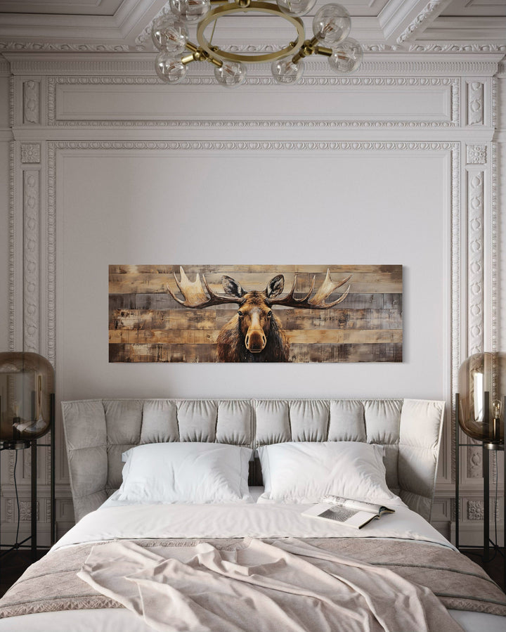 Rustic moose painting on wood-textured horizontal canvas above a bed in a neutral-toned room.