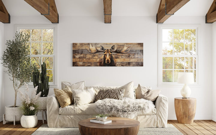 Rustic horizontal moose wall art on wood-textured canvas above a sofa in a cabin-style living room.