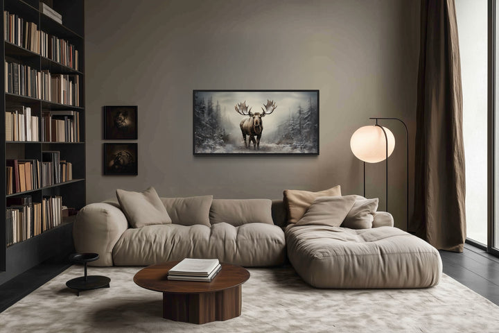 Framed moose canvas print in a rustic winter forest setting above a modern living room sofa.