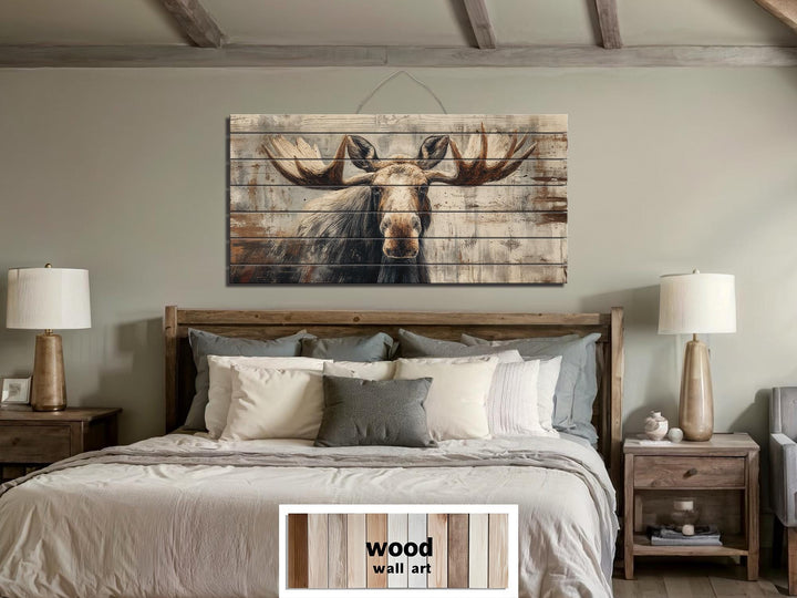 Rustic moose wall art printed on distressed wood planks hanging above a bed in a cabin-style room.