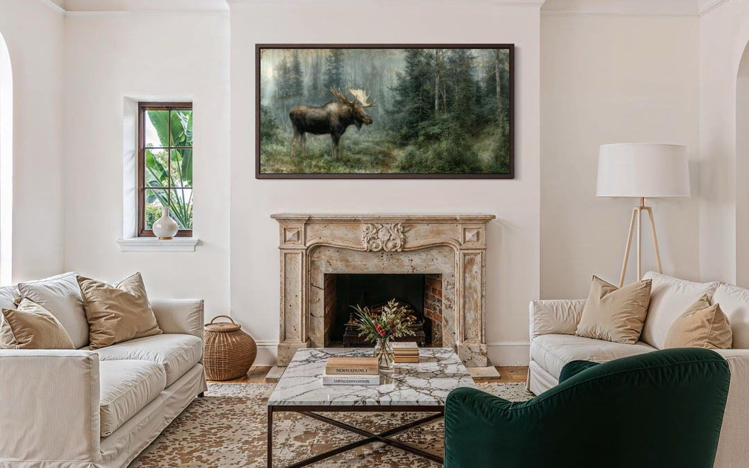 A moose canvas print in a dark wood frame hangs above a fireplace in a rustic living room.