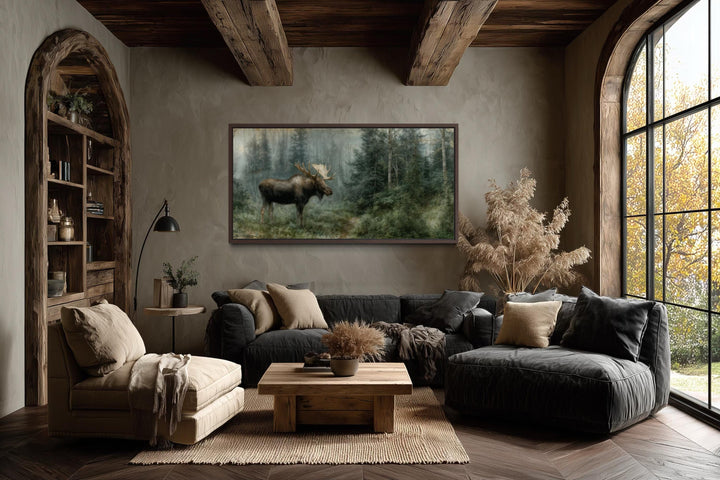 A large moose canvas print hangs in a rustic living room with dark wood beams and earthy decor.