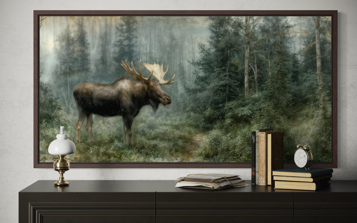 A framed canvas print of a moose in a misty forest, displayed above a dark wooden dresser.