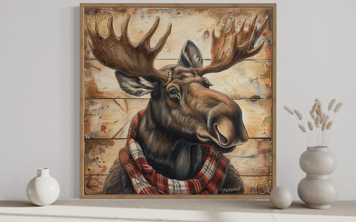 Framed canvas print of a moose wearing a red plaid scarf on a weathered wood background.