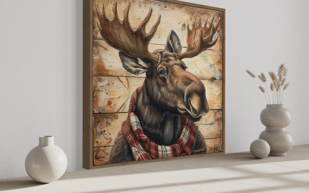 Moose with red scarf painting on weathered wood canvas print in a wooden frame on a white wall.