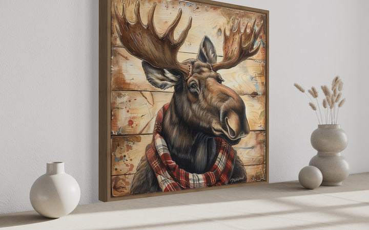 Moose with red scarf painting on weathered wood canvas print in a wooden frame on a white wall.