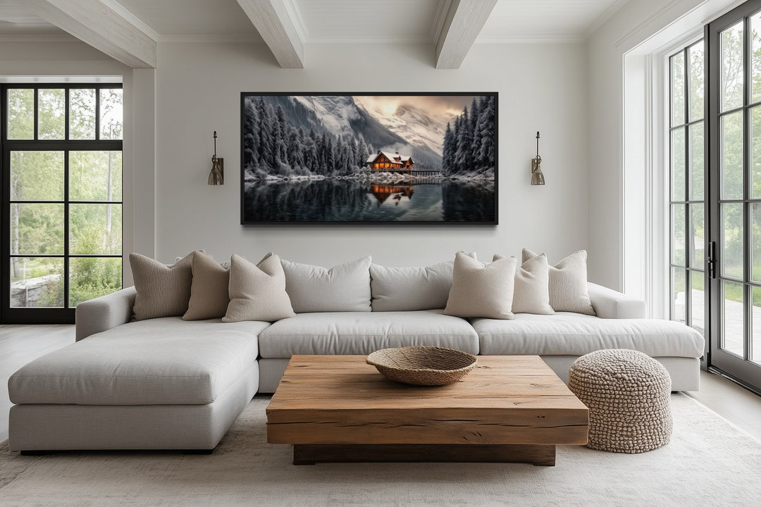 Panoramic framed canvas of a glowing winter cabin reflected in a lake, hung over a modern sofa.