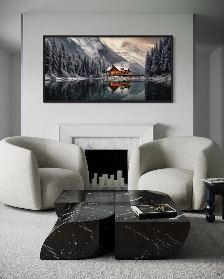 Framed panoramic canvas of a cozy winter cabin by a lake, hung above a modern white fireplace.