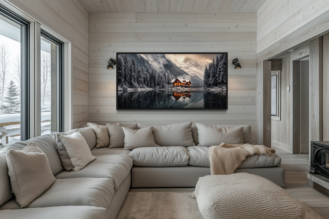 Framed panoramic canvas art of a glowing winter cabin reflected in a lake above a grey sectional.