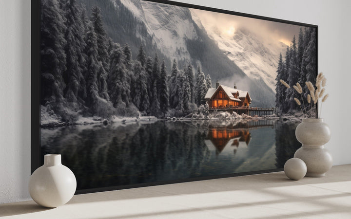 Panoramic framed canvas of a cozy winter cabin reflected in a lake with snowy mountains.